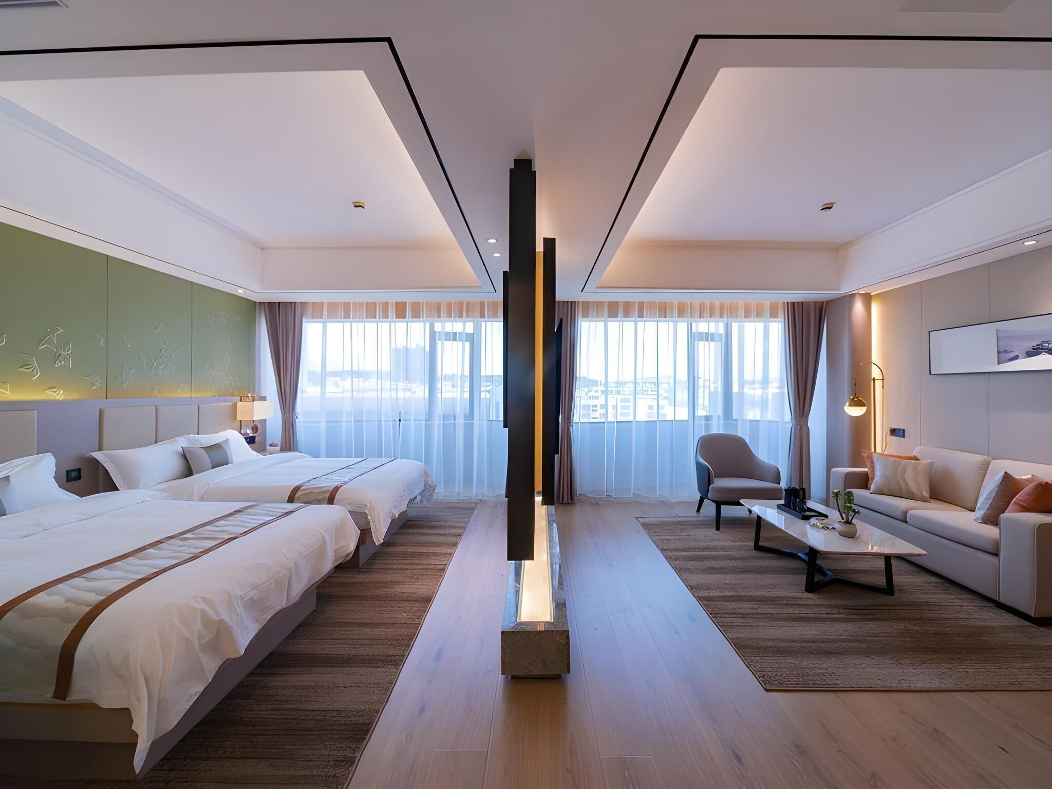 Habitación de hotel moderna con dos camas, un sofá, una mesita de café y un ventanal con vistas a la ciudad.