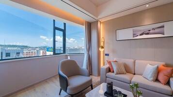 Habitació d'hotel moderna amb una finestra gran que ofereix vistes a la ciutat, un sofà confortable, un estilós butaca i una petita taula de café amb objectes decoratius.