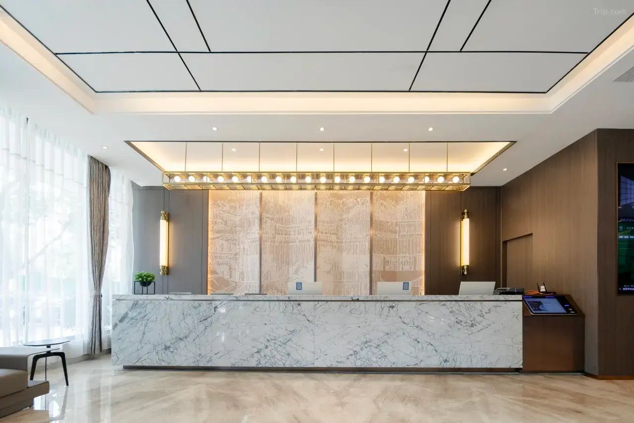Zona de recepción de hotel con mostrador de mármol, iluminación en el techo y una gran pantalla digital.