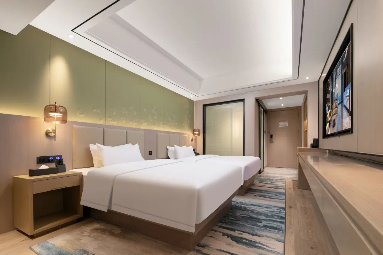 Ein Hotelzimmer mit einem großen Bett, Nachttischen, einem Schreibtisch und einem großen Fenster.