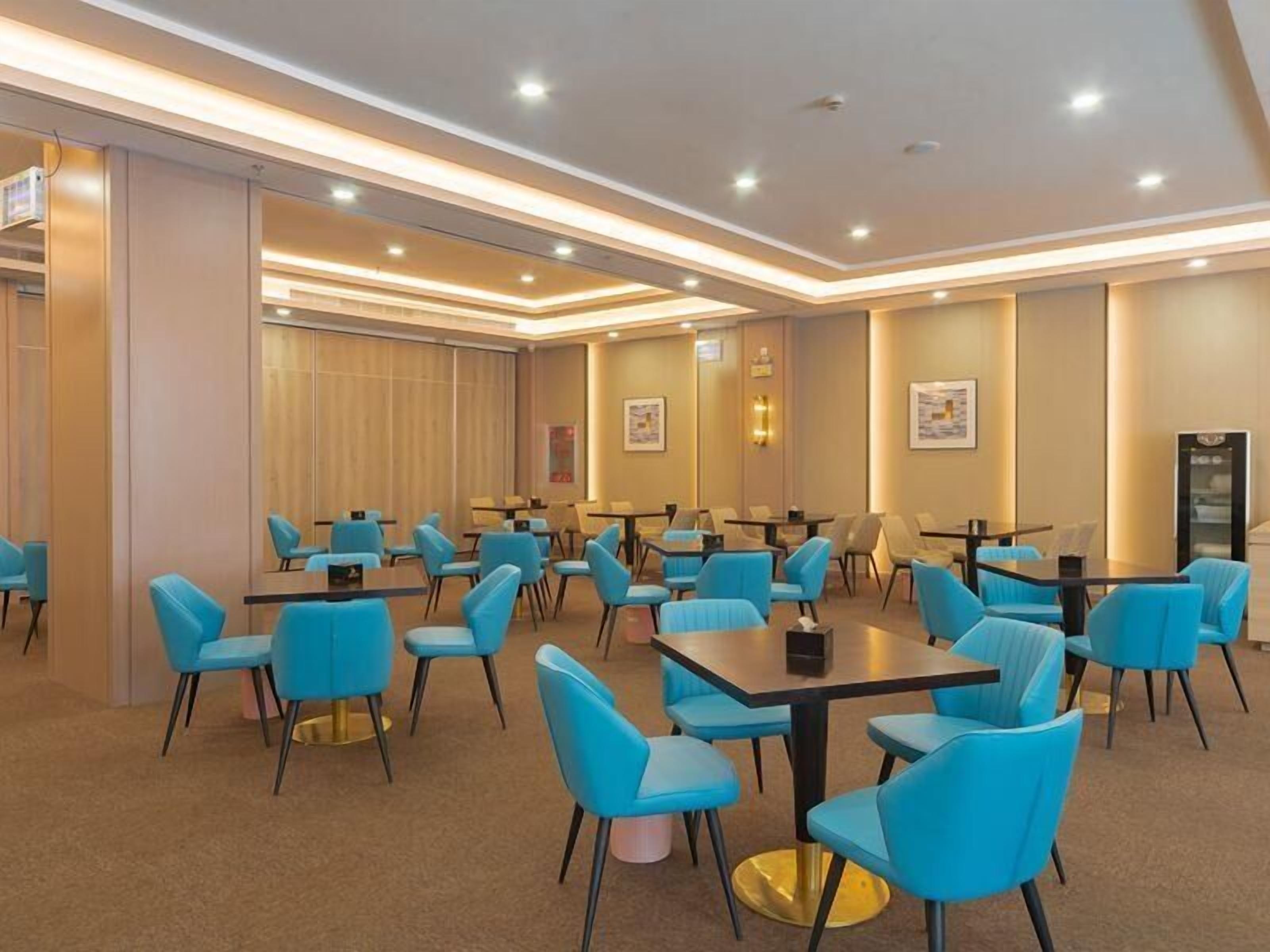 Un salón de conferencias de hotel con varias mesas y sillas azules, equipado con luces en el techo e imágenes enmarcadas en las paredes.