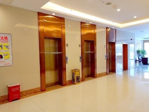 Un vestíbulo de hotel con cuatro ascensores, un cesto de basura y una mesa de recepción.