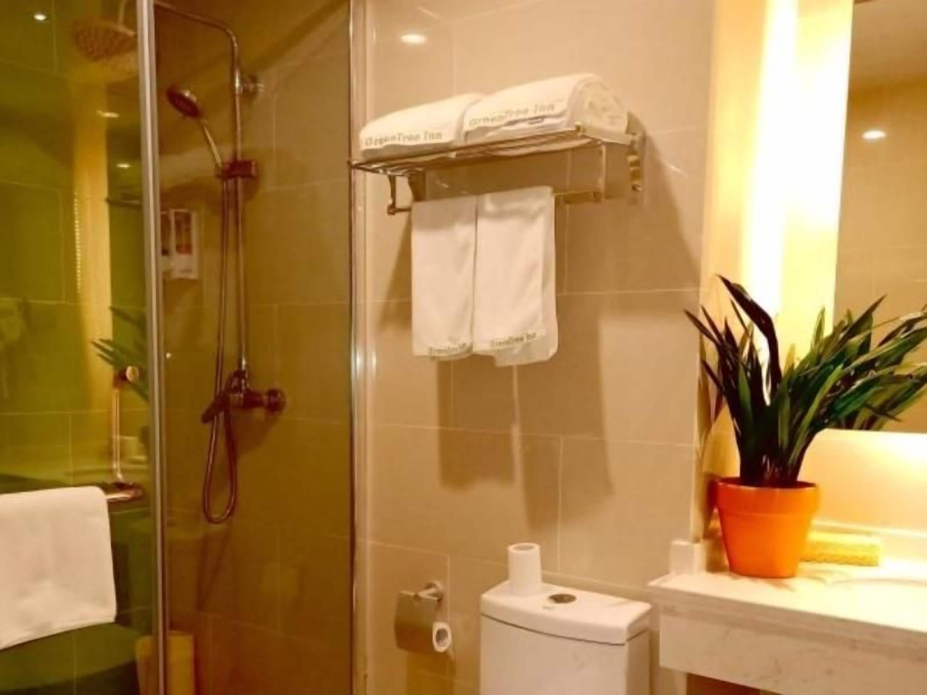 A bathroom with a glass-enclosed shower, a toilet, a sink with a potted plant, and a towel rack with towels.