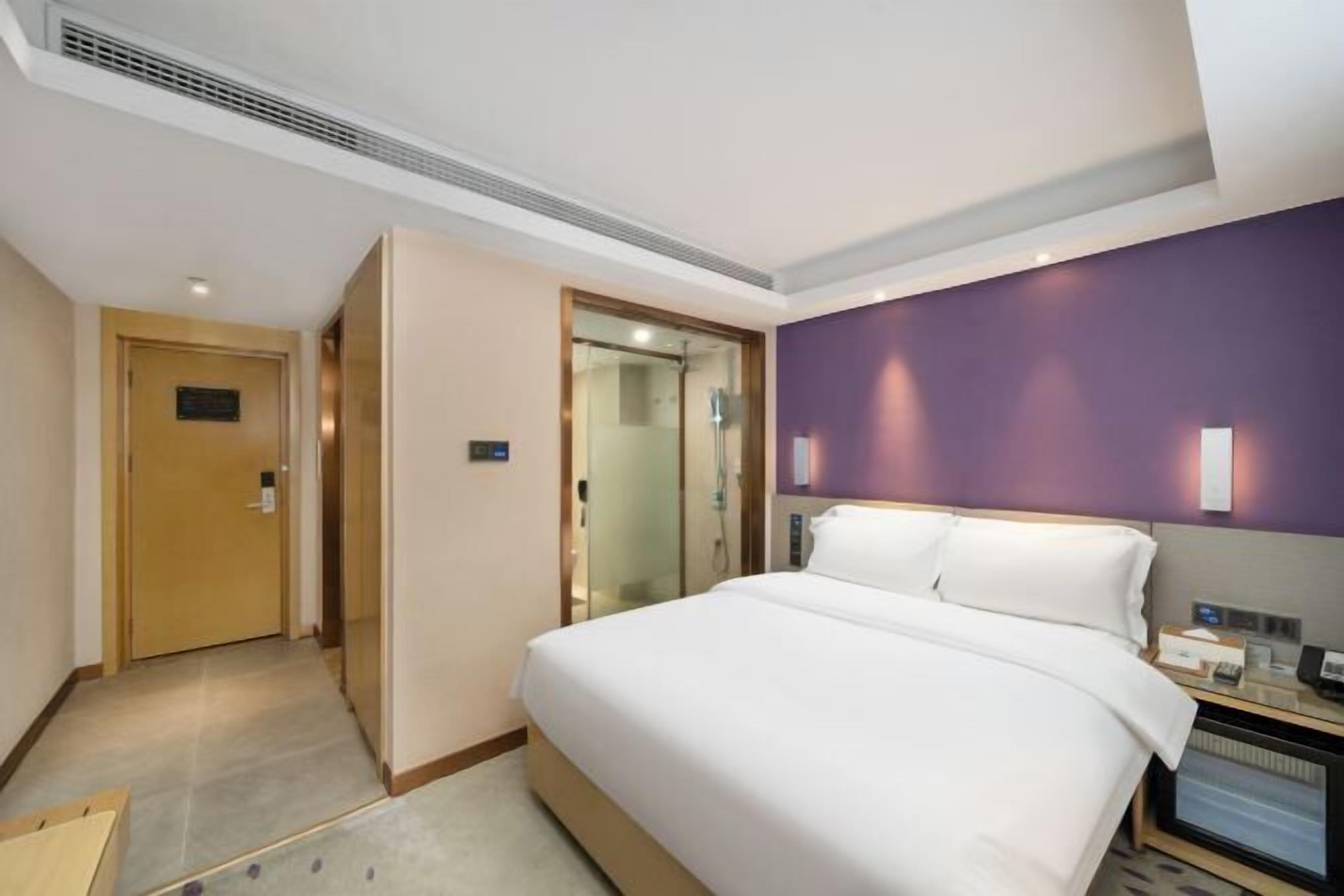 A hotel room with a bed, a desk, a chair, a nightstand, a lamp, and a door.