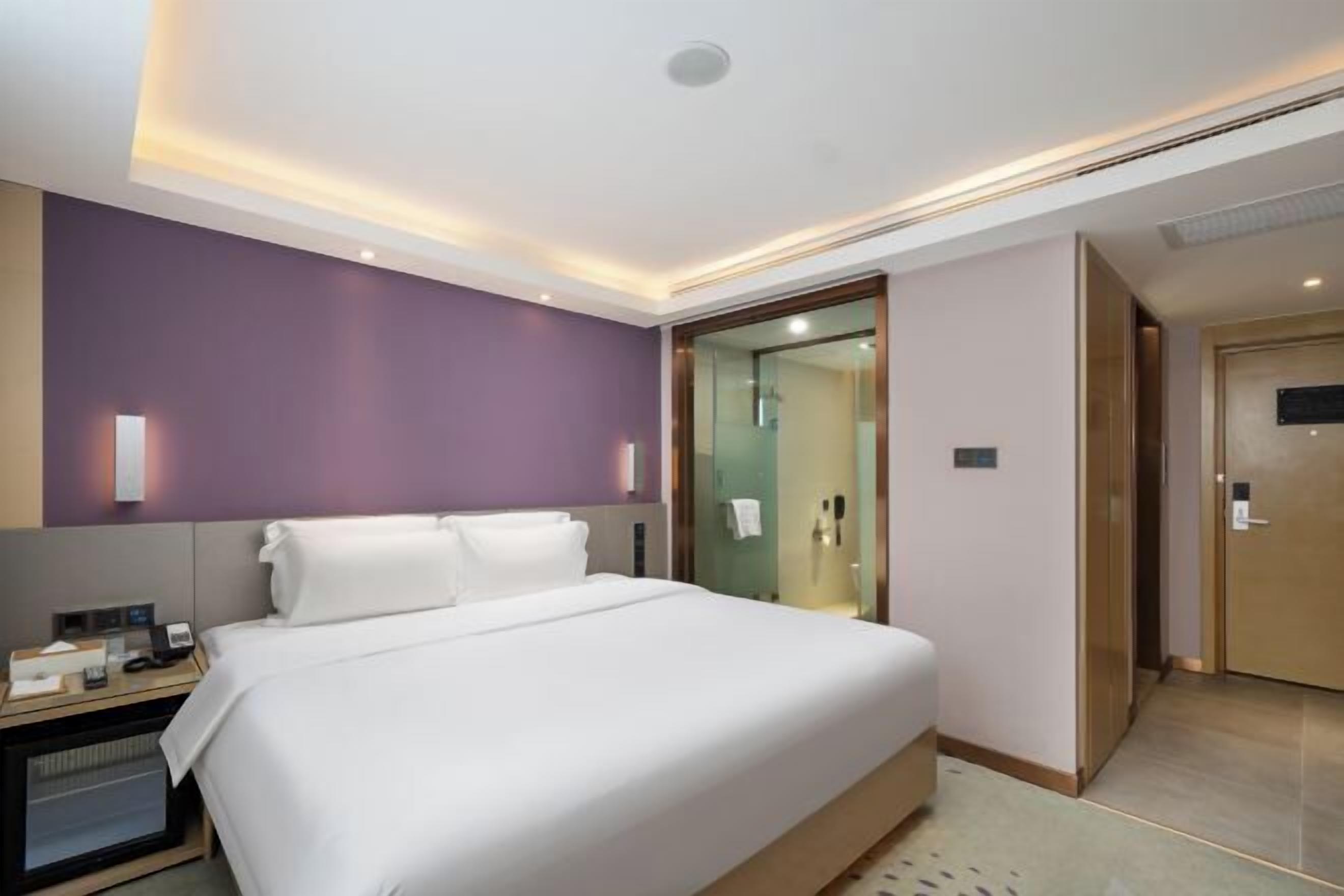 Et moderne hotelværelse med en stor seng, et sengebord med telefon og lampe, samt en glasdør til et badeværelse.