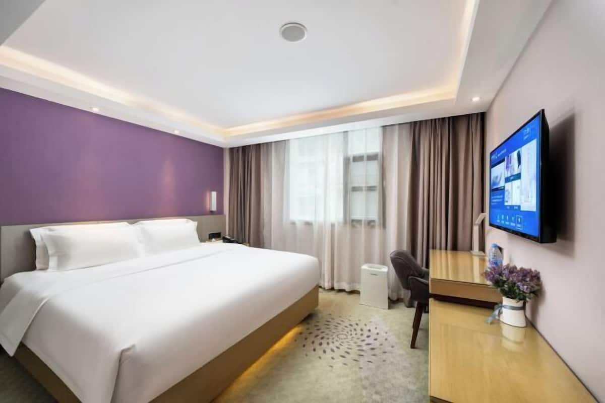 A hotel room with a bed, a desk, a TV, and a window with curtains.