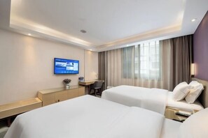 Ein Hotelzimmer mit zwei Betten, einem Schreibtisch, einem Fernseher und einem Fenster mit Vorhängen.