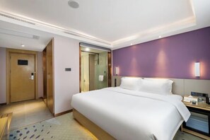 Ein Hotelzimmer mit einem großen Bett, einem Nachttisch, einem Spiegel und einer Tür zu einem weiteren Raum.