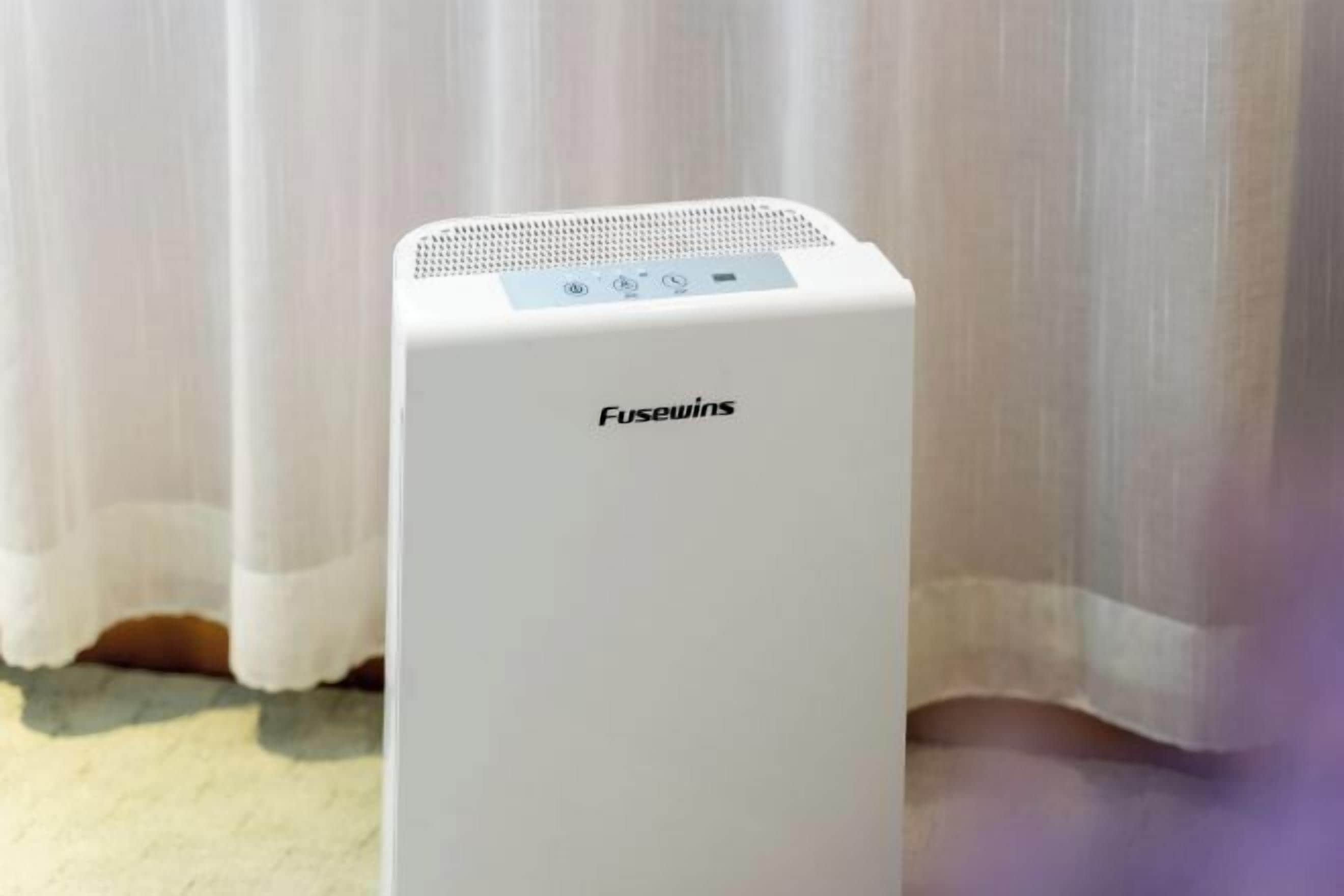 A white Fusewins portable heater in a room with a white curtain backdrop.