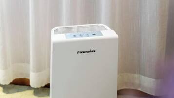 A white Fusewins portable heater in a room with a white curtain backdrop.