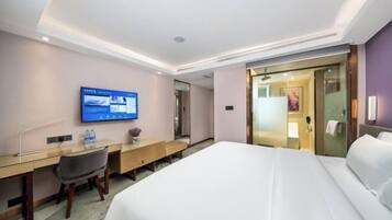 A hotel room with a bed, desk, chair, television, and a bathroom visible through a glass door.