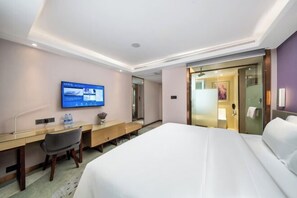 Ein Hotelzimmer mit Bett, Schreibtisch, Stuhl, Fernseher und einem durch eine Glastür einsehbaren Badezimmer.