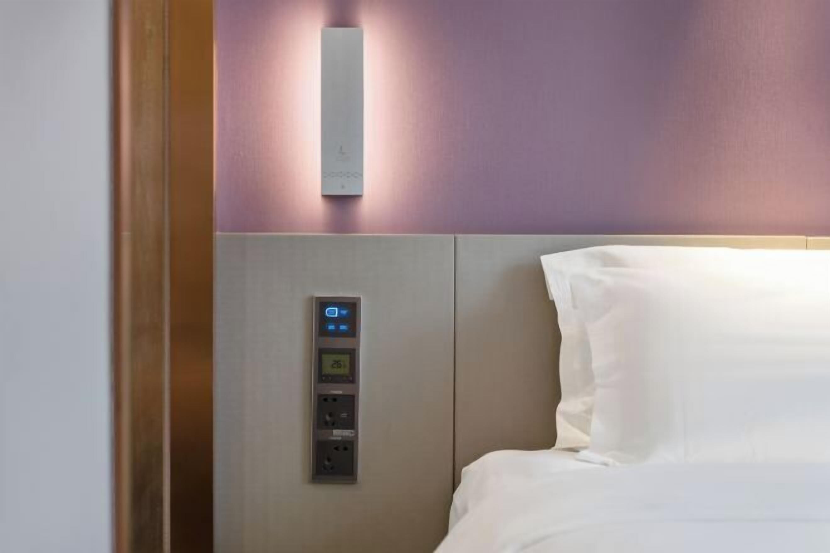 A hotel room with a bed, a control panel, and a wall-mounted light fixture.