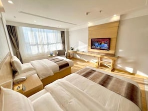 A hotel room with two beds, a TV, a desk, and a window with curtains.