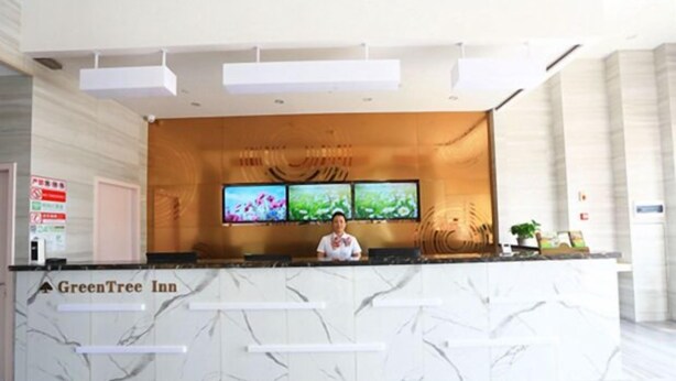 Una recepción en el GreenTree Inn con diseño de mármol, dos monitores encima y una recepcionista.