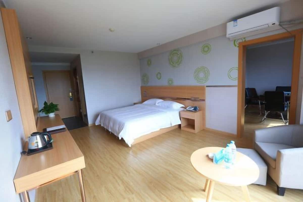 A hotel room with a bed, bedside table, chair, and a small table with a water bottle.
