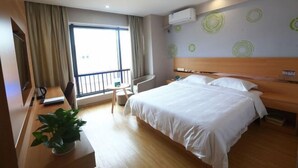 Una habitación de hotel con cama, escritorio, silla, planta en maceta y ventana con cortinas.