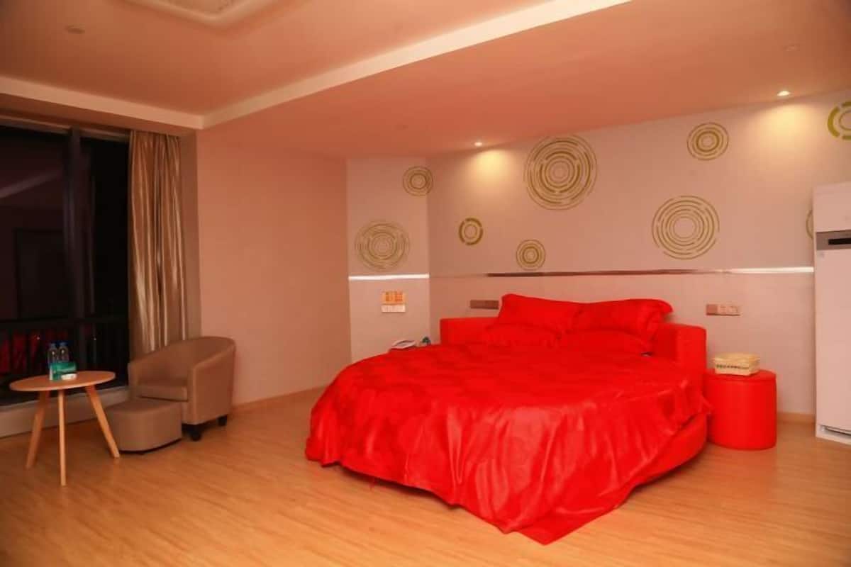 A modern hotel room with a large bed, a small table, a chair, and a red accent wall.