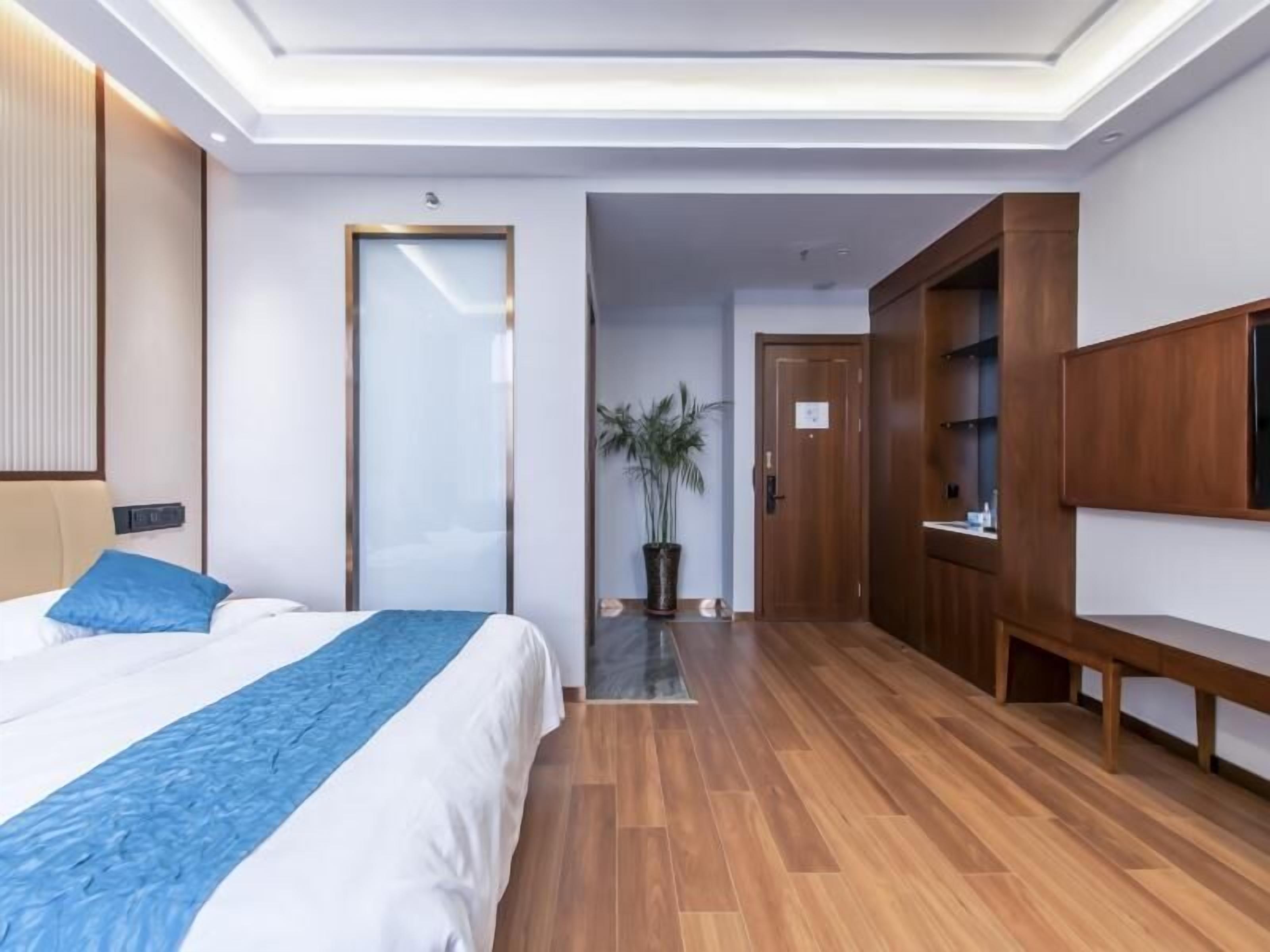 Una habitación de hotel moderna con una cama grande, suelo de madera, un televisor y un armario.