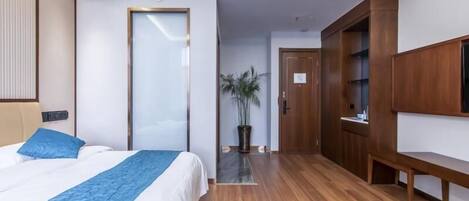Una habitación de hotel moderna con una cama grande, suelo de madera, un televisor y un armario.