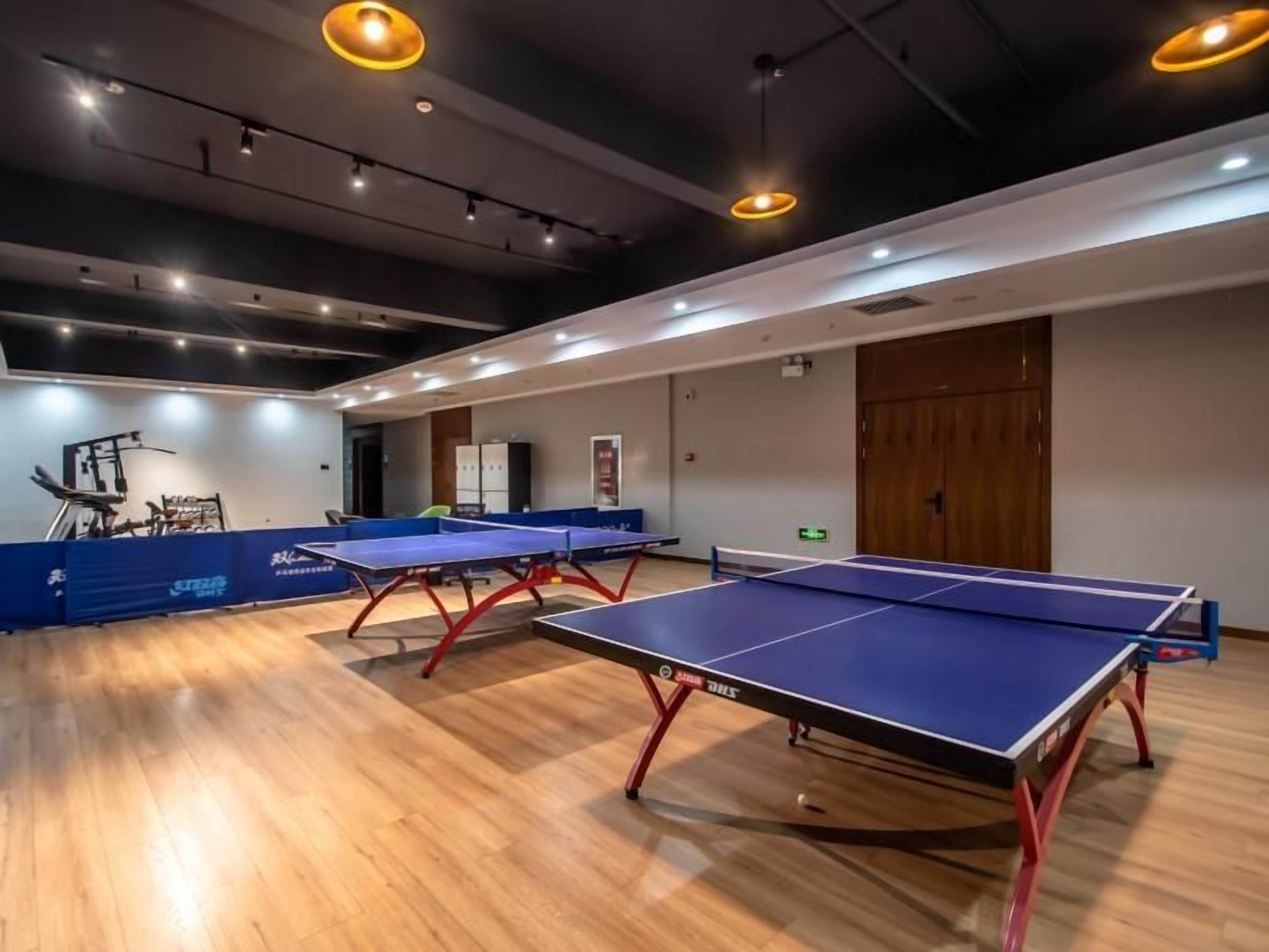 A room with ping pong tables, wooden flooring, and recessed lighting.