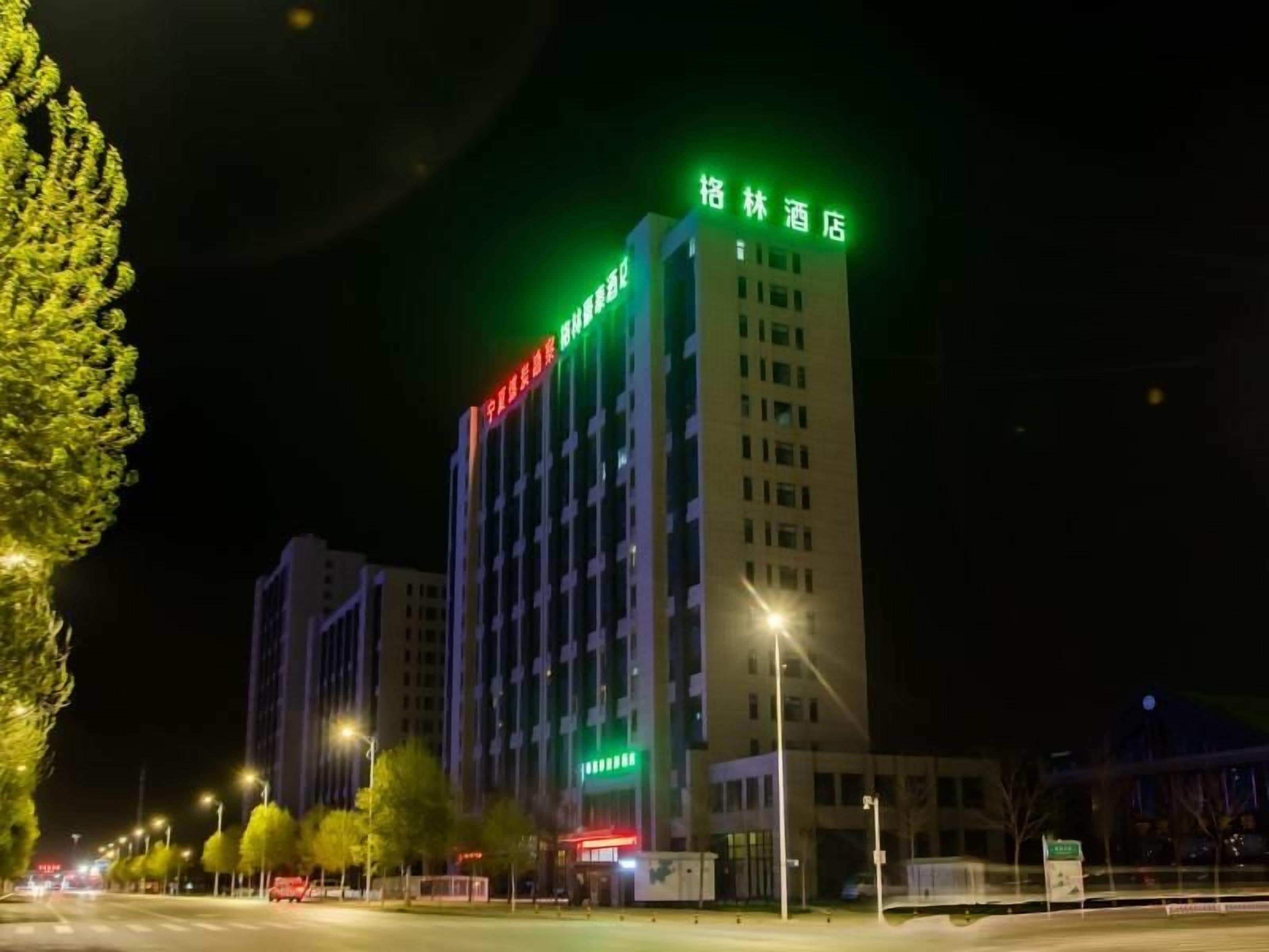 A hotel with a modern design, featuring a prominent green sign at the top.
