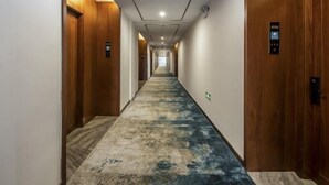 Un pasillo de hotel con puertas de madera, una alfombra estampada y una lámpara en el techo.