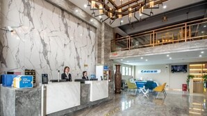 Zona de recepción de hotel con paredes de mármol, mostrador de recepción y área de estar con sillas.
