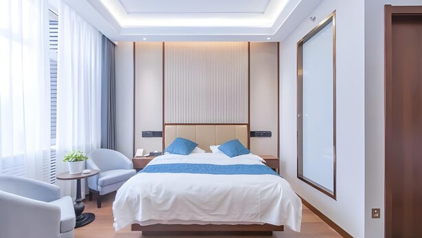 Una habitación de hotel moderna con una cama grande, una mesita de noche, una silla y un ventanal con cortinas.