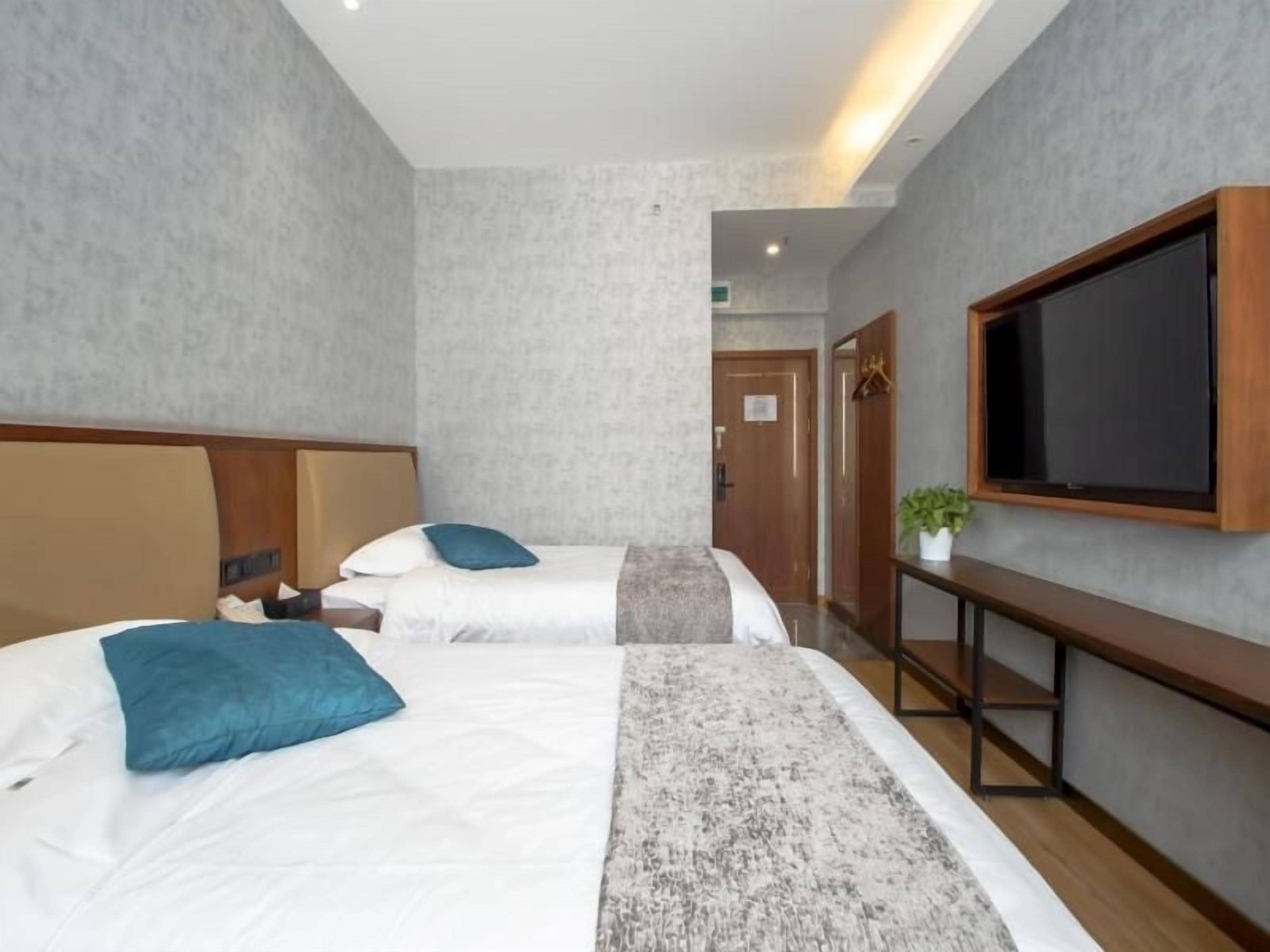 Ein Hotelzimmer mit zwei Betten, einem an der Wand montierten Fernseher und einem kleinen Tisch mit einer Pflanze.