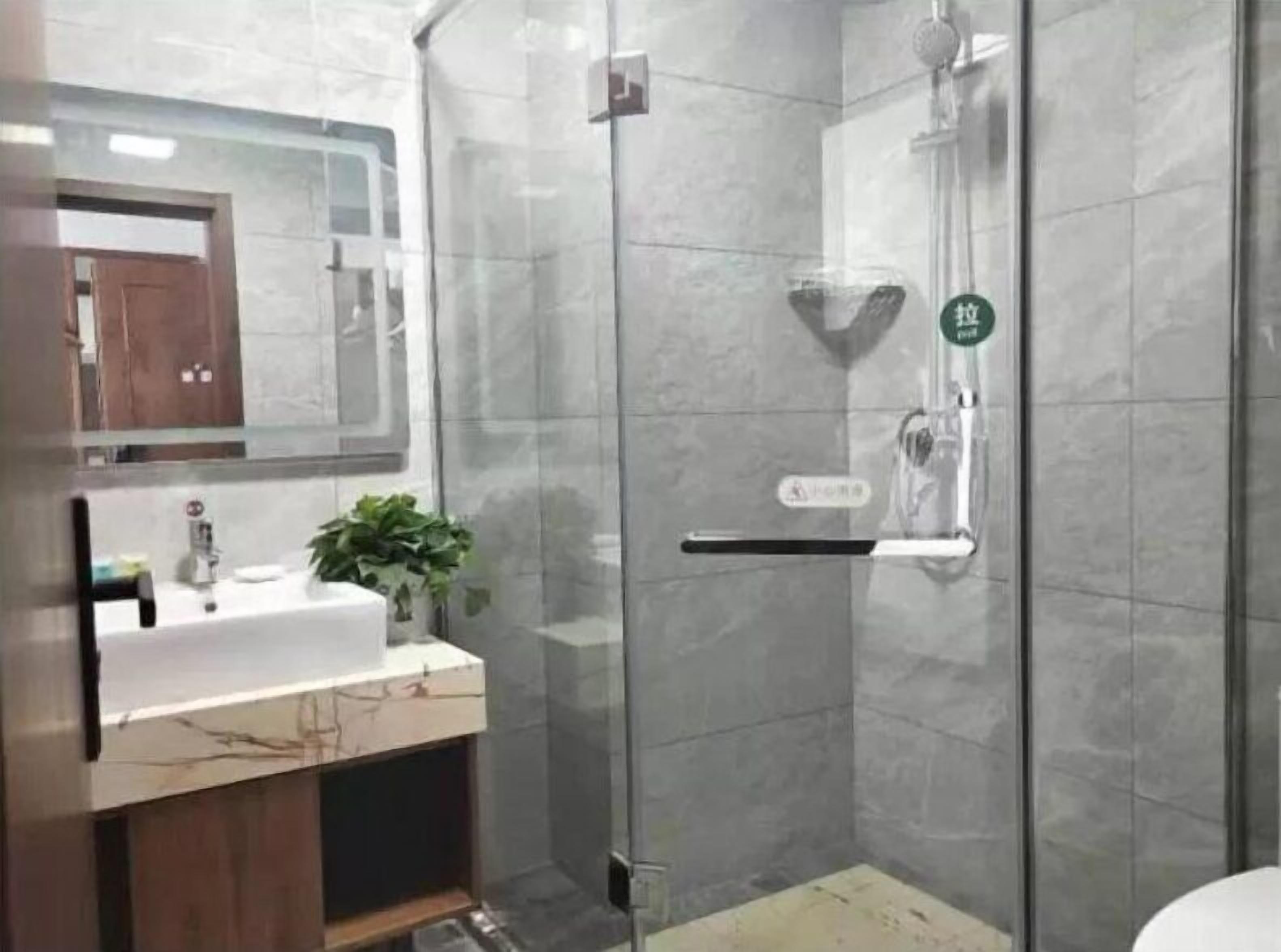 A modern bathroom with a glass-enclosed shower, a sink with a mirror above it, and a potted plant on the counter.