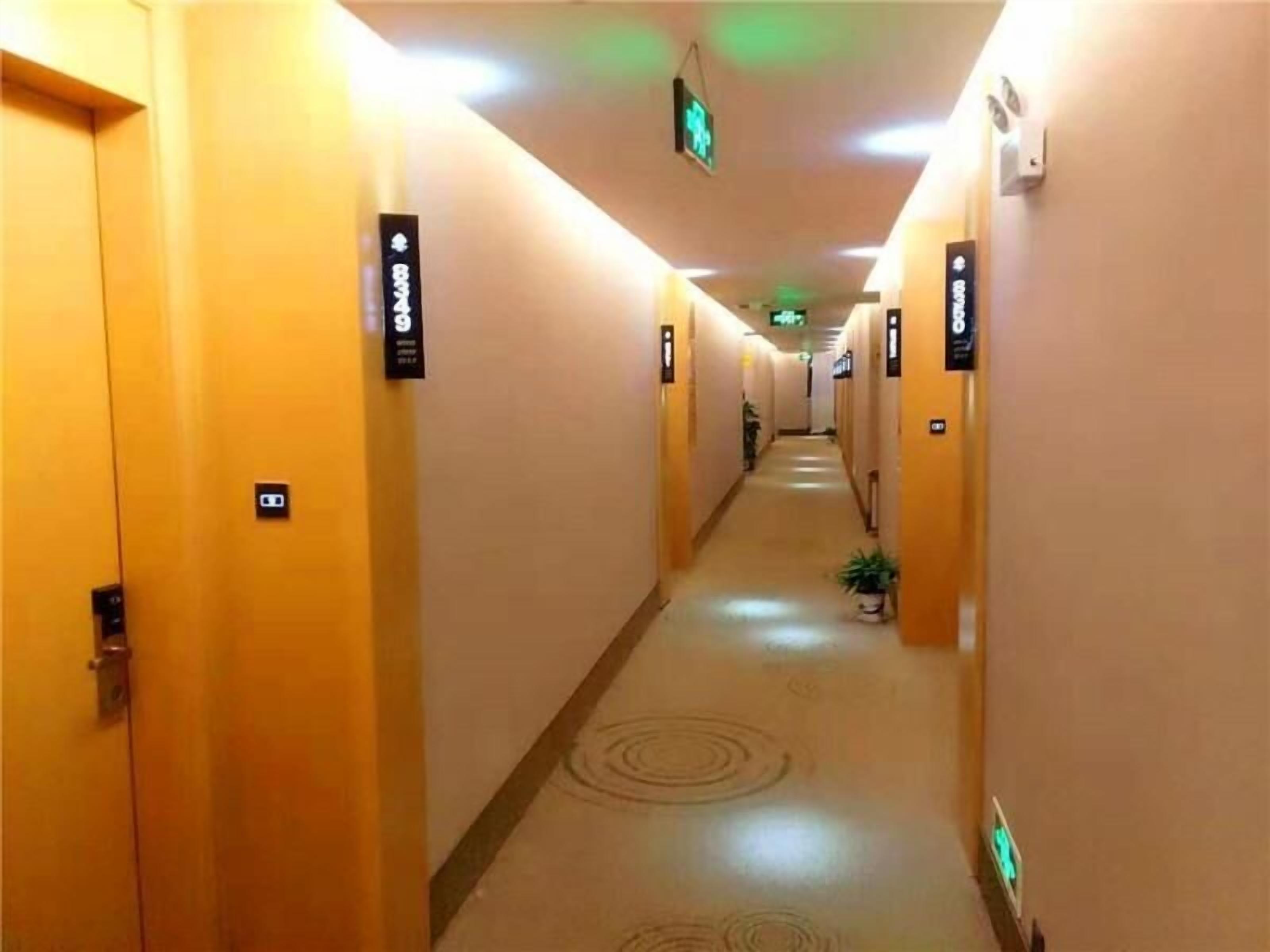 A hotel hallway with doors marked with room numbers, a patterned carpet, and a green exit sign.