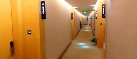 A hotel hallway with doors marked with room numbers, a patterned carpet, and a green exit sign.