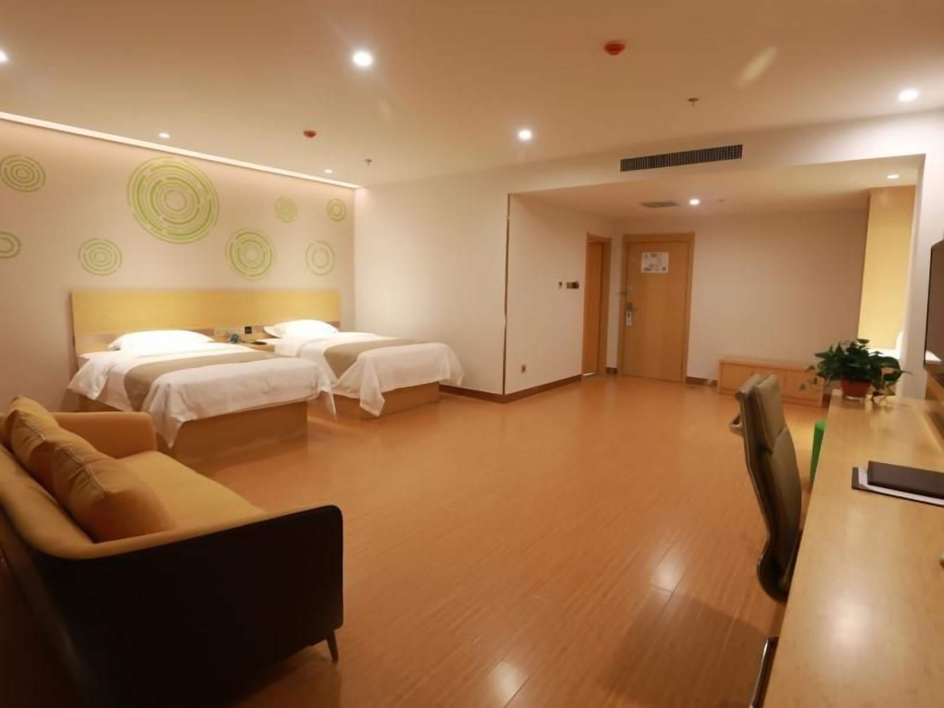 A hotel room with two beds, a sofa, a desk, and a potted plant.