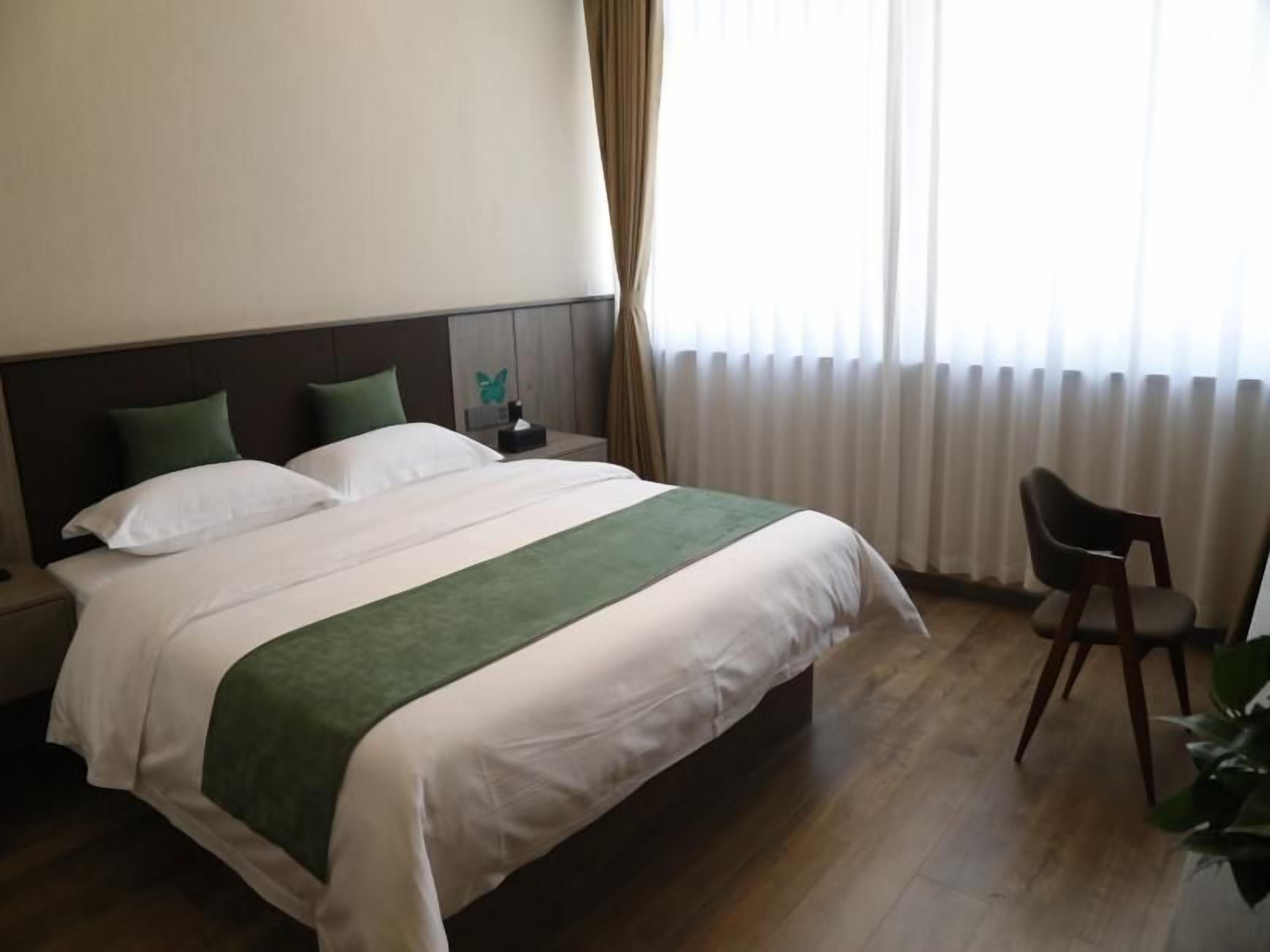 A hotel room with a bed, a nightstand, a chair, and a window with curtains.