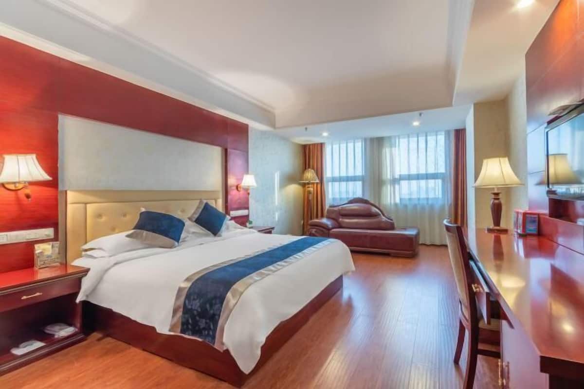 A hotel room with a large bed, a leather armchair, a desk, and a window with curtains.