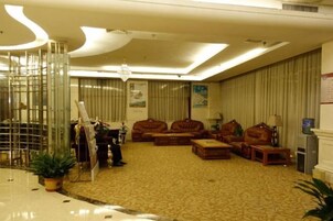 Un vestíbulo de hotel con alfombra estampada, sofás de cuero, una araña y una recepción.