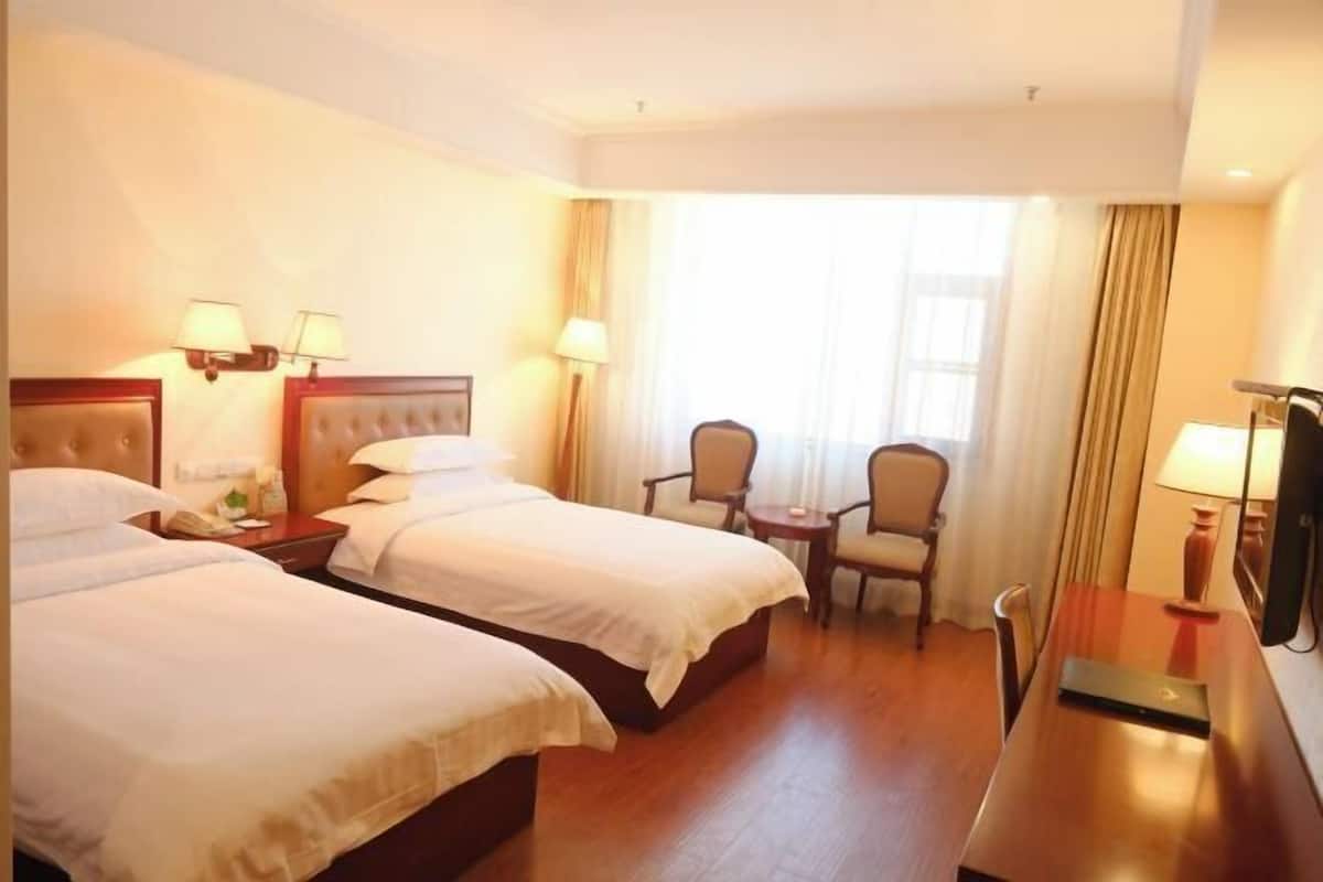 A hotel room with two beds, a desk, a chair, and a TV.