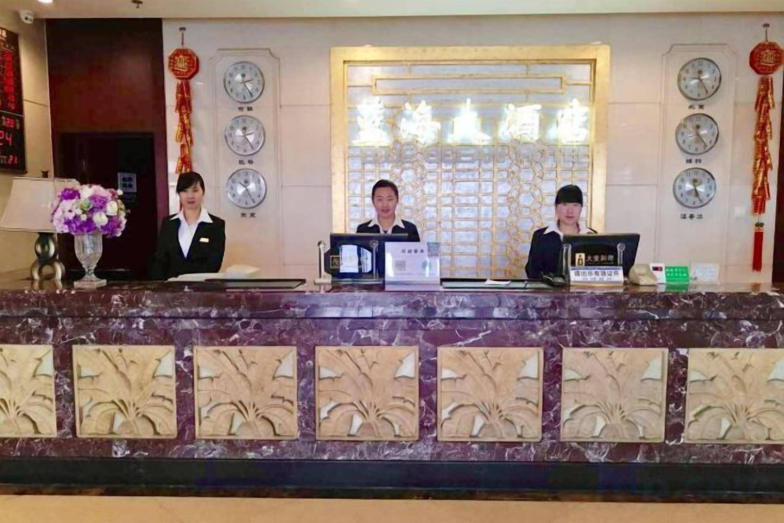 A reception desk with three staff members, a clock, and a decorative wall.