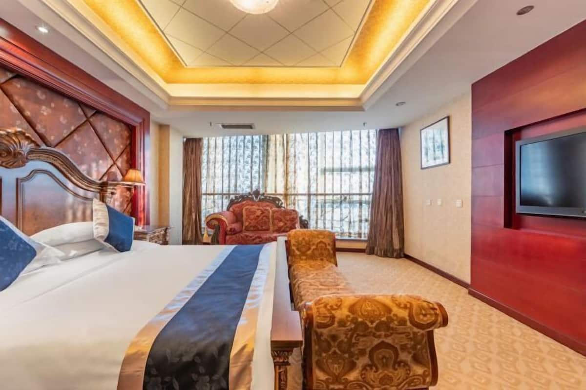 A hotel room with a large bed, a sofa, a TV mounted on the wall, and a window with curtains.