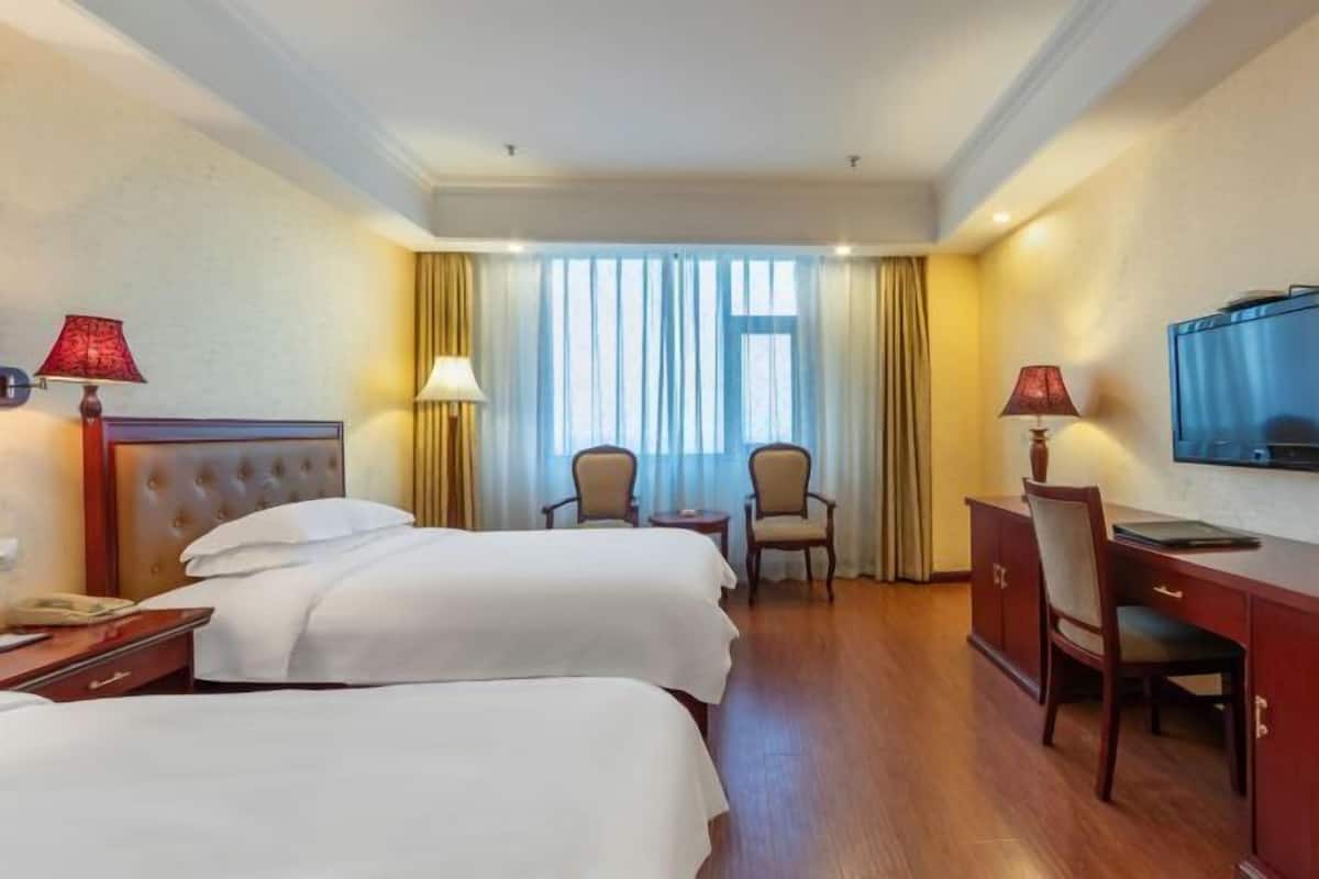 A hotel room with two beds, a desk, a chair, a TV, and a window with curtains.
