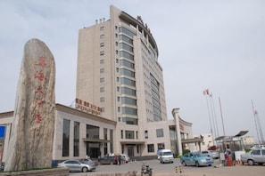 Un edificio de varios pisos con una entrada destacada y un gran monumento de piedra.