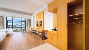 A hotel room with a bed, a desk, a wardrobe, and a view of the city through large windows. - GreenTree Inn (Qionghai Boao High-speed Railway Station) (Qionghai)