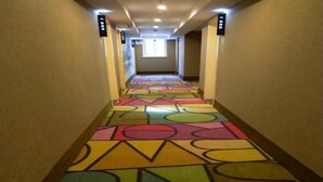 Un couloir agrémenté d’un tapis aux motifs géométriques et colorés, de luminaires fixés au mur et d’une fenêtre au fond.