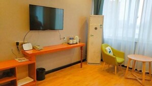 Une chambre d’hôtel avec un plancher en bois, un téléviseur fixé au mur, un bureau avec un téléphone, un réfrigérateur, une chaise jaune et une petite table ronde.