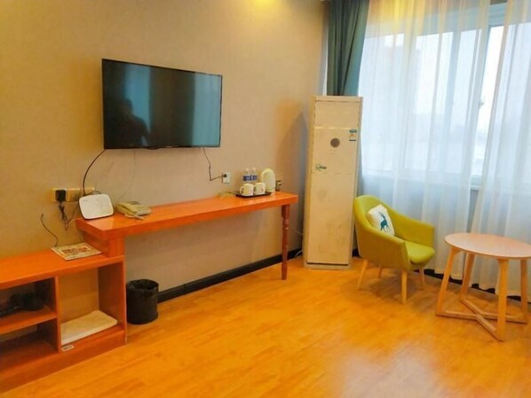 A hotel room with a wooden floor, a TV mounted on the wall, a desk with a telephone, a refrigerator, a yellow chair, and a small round table. - Shell Kaifeng City Lancao County Women and Children Hospital Hotel (Kaifeng)