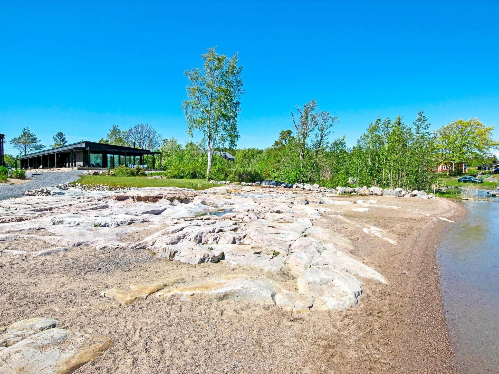 Une plage de galets avec un bâtiment moderne et des arbres en arrière-plan.