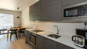 A modern kitchen with dark cabinetry, a built-in microwave, a coffee maker, and a dining area with a table and chairs. - Kasnäs marina b11 by Interhome (Kemiönsaari)
