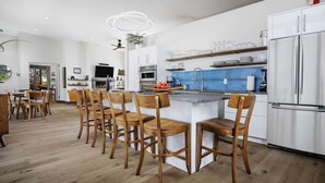 A modern kitchen with a central island, wooden chairs, and a built-in refrigerator. - Modern Custom Vineyard Cottage, Epic Views, Huge Decks, BBQ, Ping Pong, EV Charger, Walk to Wineries (Dundee)
