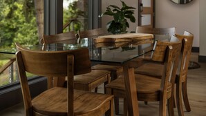 A dining area with a glass table and wooden chairs, a plant, and a view of trees outside. - Modern Custom Vineyard Cottage, Epic Views, Huge Decks, BBQ, Ping Pong, EV Charger, Walk to Wineries (Dundee)